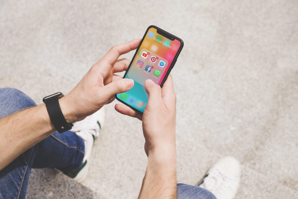Vista aérea de la mano del hombre usando la aplicación de medios sociales en el móvil 2020